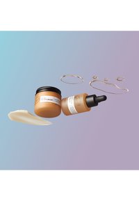 Deux produits de soin de la peau sur un fond dégradé : un pot marron de crème hydratante, un flacon compte-gouttes de sérum, avec des accents de crème et d'or.