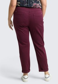 Pantalones burdeos de corte relajado, con dobladillos ajustados y dos bolsillos traseros. Hechos de una tela suave, con una textura lisa y líneas limpias.