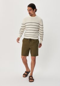 White striped sweater with navy stripes, olive green shorts, and brown sandals. Loose fit, casual design, with drawstring waist on shorts.