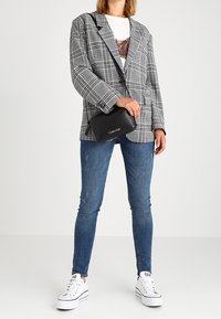 Šedý kostkovaný blazer, bílý tričko, černá crossbody taška, modré skinny džíny a bílé platformové tenisky. Ležérní, vrstvený outfit.