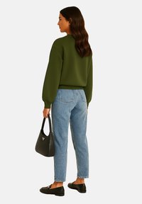 Olijfgroen sweatshirt met doorgezakte schouders, gecombineerd met lichtblauwe spijkerbroek. Zwarte instappers en een kleine zwarte handtas maken de look compleet.