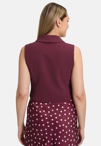 Ärmelloses, cropped Top aus burgunderfarbenem Stoff mit Kragen, kombiniert mit einem Rock, der große, cremefarbene Tupfen auf burgunderfarbenem Hintergrund aufweist.