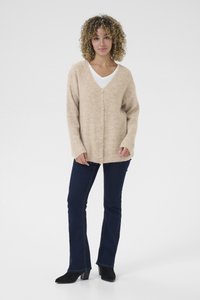 Beige stickad kofta med V-hals, långa ärmar och fem knappar, i kombination med mörkblå utsvängda jeans och svarta klackboots.