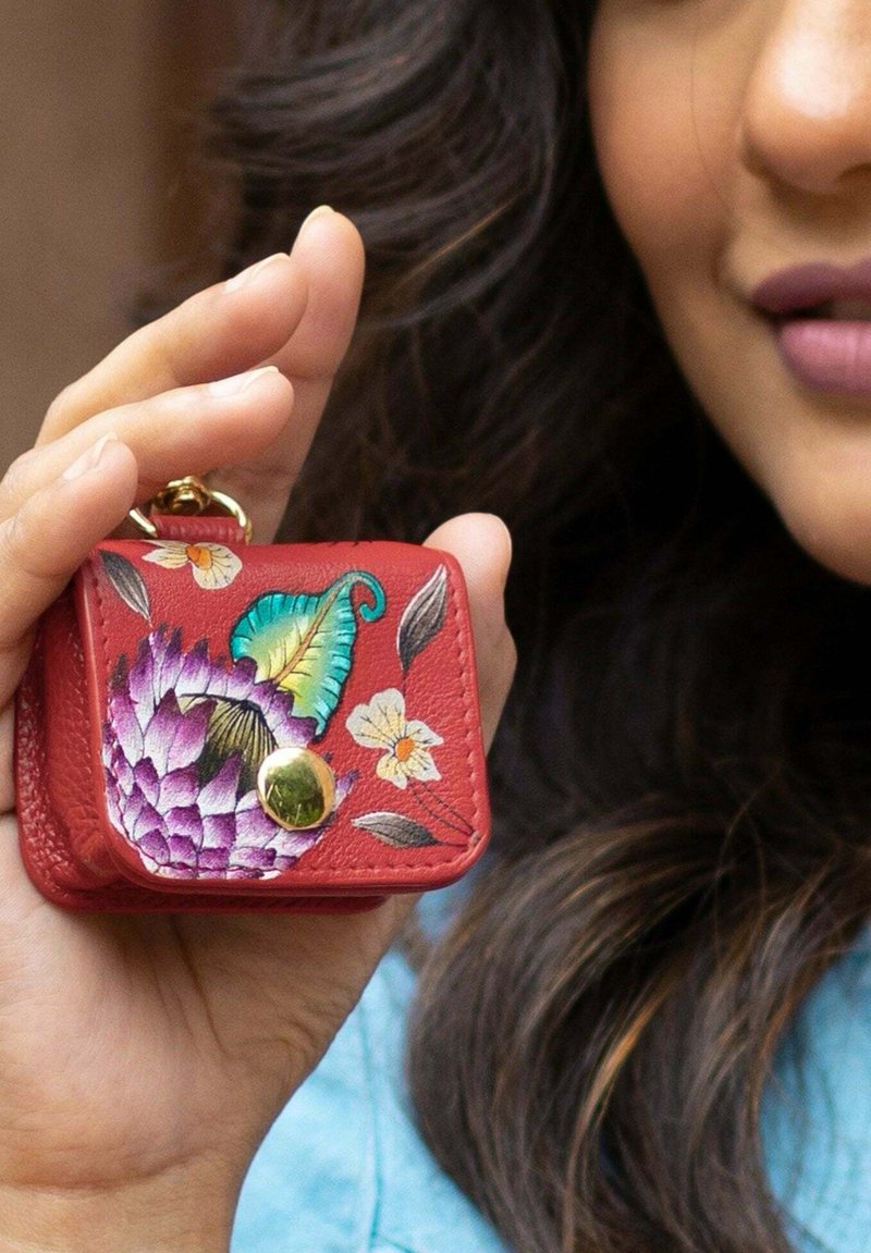 Rode leren muntenpouch met bloemen- en bladenborduurwerk. Heeft een ronde vorm, drukknopensluiting en een groene accentknop.