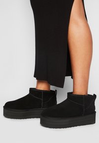 Botas negras de ante hasta el tobillo con suela plataforma y detalles de costura. Cuentan con una lengüeta en la parte trasera y suela de goma texturizada.