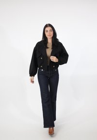 Sort cropped jakke med oversized ærmer og dobbeltradede guldknapper; kombineret med tætsiddende beige top og vidde mørk denimjeans.