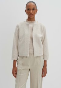 Hellbeige cropped Jacke aus einem weichen Wollmischung, mit rundem Ausschnitt, zwei Seitentaschen und drei Viertel-Ärmeln.