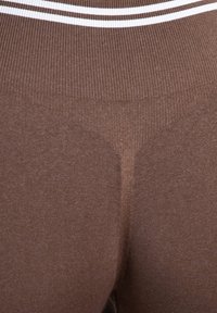 Leggings marron taille haute en tissu côtelé, avec une bande blanche accentuée en haut et une finition texturée et lisse.
