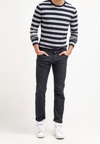 Randig grå och marinblå långärmad skjorta, svarta byxor och vita sneakers. Slim fit, avslappnad design med rundad halsringning och ribbade ärmslut.