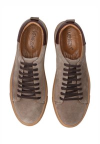 Zamszowe sneakersy w jasnoszarym kolorze z brązowymi akcentami i teksturowaną skórzaną podszewką. Posiadają ciemnobrązowe sznurowadła i gumową podeszwę.