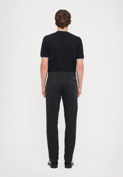 Polo bleu marine à manches courtes, avec des accents bleu clair, associé à un pantalon noir slim. Texture de tissu lisse, détails de design minimalistes.