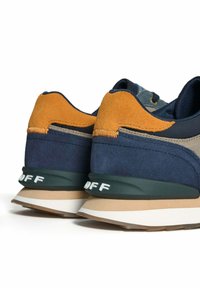 Ein Paar blaue und sandfarbene Wildledersneaker mit beigen und weißen Sohlen, von hinten auf einem weißen Hintergrund betrachtet.