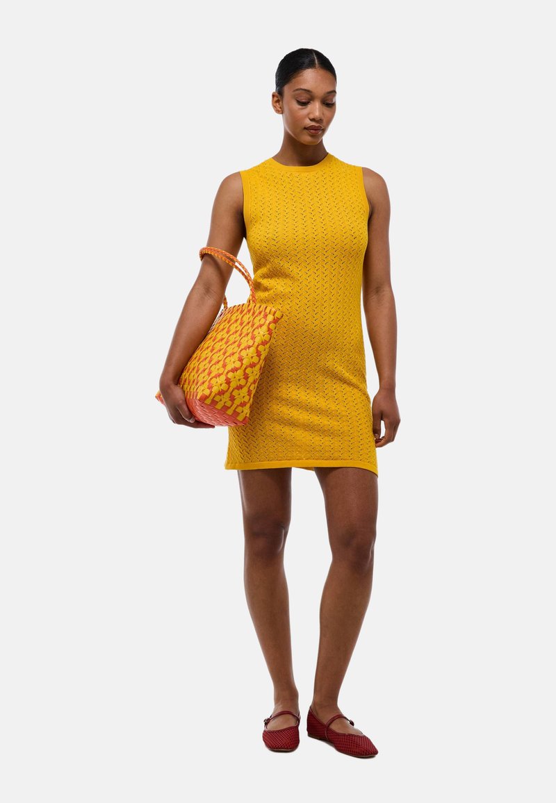 Robe en tricot jaune avec une silhouette ajustée, un col rond et un motif texturé. Chaussures rouges et un sac à main à motifs rouge et jaune.