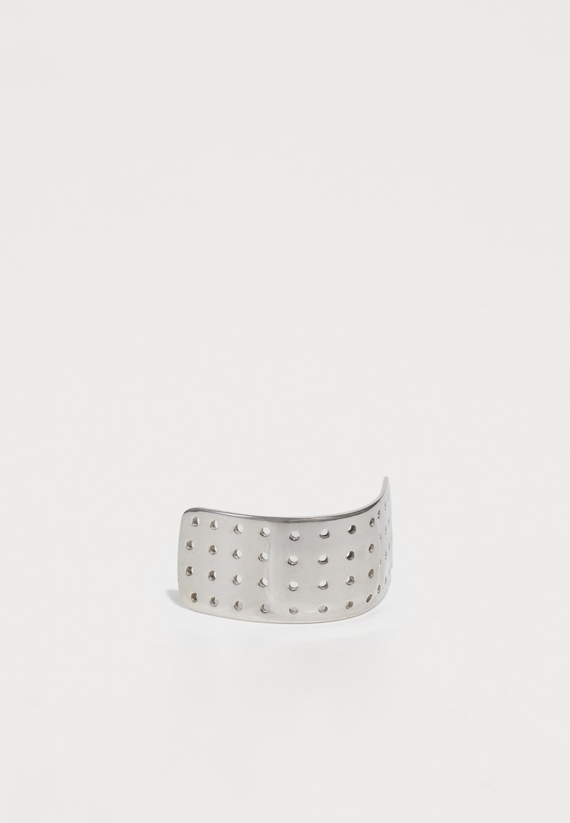 Stříbrný kovový náramek ve tvaru prstenu s křivkovým designem a rovnoměrně rozmístěnými otvory na celém povrchu. Hladký povrch s lesklým finišem.