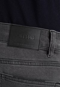 Grå jeans i denim med en strukturerad läderpatch märkt "ONLY & SONS", med standardmidjeband och kontrasterande sömmar.