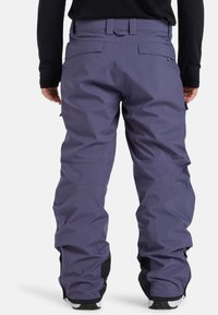 Pantalones de nieve impermeables de color púrpura con un corte holgado, cinturilla elástica y puños con cremallera. Presenta múltiples bolsillos para almacenamiento.
