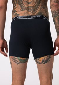 Dark navy boxer shorts with a logoed waistband. The fabric appears smooth, featuring a snug fit and mid-thigh length. Detailed tattoos visible.