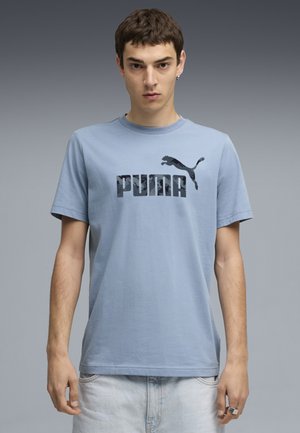 Lyseblå bomulds t-shirt med et iøjnefaldende sort "PUMA" logo og et hoppe-puma grafik. Korte ærmer og rund halsudskæring.