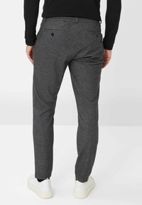 Grijze, gestructureerde broek met een elastische tailleband, zijzakken en achterzakken met knoop, gecombineerd met witte sneakers.
