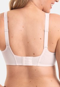 Beige bra with adjustable straps, textured fabric, and a hook-and-eye closure at the back. Features delicate detailing on straps.