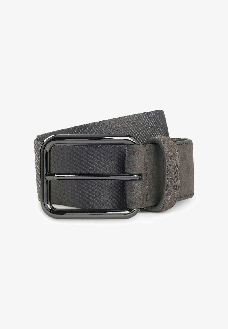 Grijze stoffen riem met een matte afwerking, voorzien van een rechthoekige zwarte metalen gesp en een suède-achtige textuur bij de bandbevestiging.