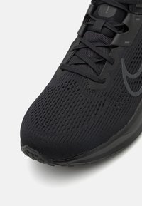 Chaussure de course Nike avec un dessus noir et texturé, présentant un design en maille et un système de laçage, complété par une semelle lisse en caoutchouc.