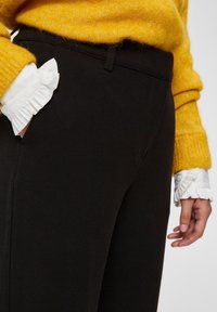 Czarne spodnie o dopasowanym kroju, z bocznymi kieszeniami. Połączone z teksturowanym żółtym swetrem oraz białymi falbankami przy mankietach bluzki.