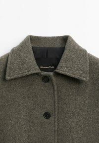 Gros plan d’un manteau en laine gris avec un large col et deux boutons noirs visibles à l’avant.