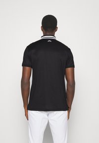 Svart polo skjorta med kontrasterande vit krage, korta ärmar och en mjuk textur; logotypen finns på baksidan av halsområdet.