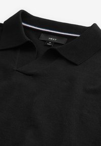 Polo noir avec col en V et manches courtes. Tissu texturé avec un col orné d'une bande colorée sur le bord.