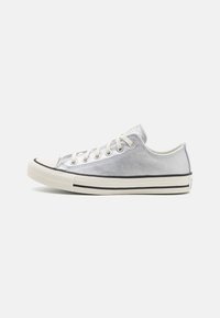 Stříbrná nízká sneakers s texturovaným povrchem, gumovou špičkou, černými akcenty a bílou podrážkou. Obsahuje šněrování na očkách a měkkou podšívku.