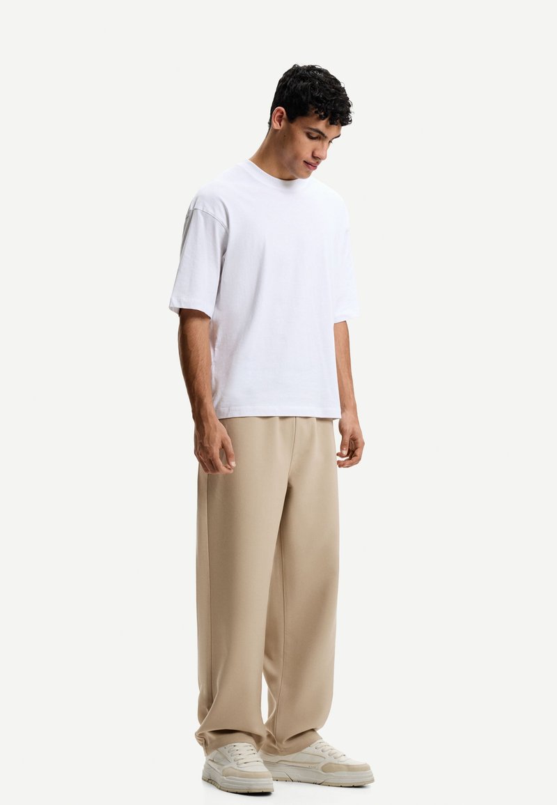 T-shirt en coton blanc à manches courtes, associé à un pantalon large beige et des baskets blanches. Look simple et décontracté avec un col rond.
