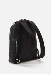 Sac à dos en cuir noir avec une finition texturée, deux poches avant zippées et des bretelles en tissu ajustables.