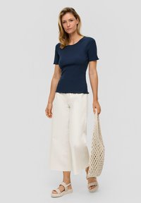 Marineblauwe geribbelde top met korte mouwen en een ronde hals, gecombineerd met off-white wijde broek en een getextureerde crèmekleurige tas, gedragen met chunky sandalen.