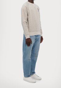 Gray sweatshirt with a round neckline, features a small colorful embroidered design. Worn with light blue loose-fit jeans and white sneakers.