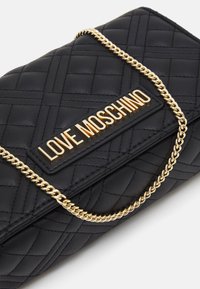 Borsa a tracolla nera trapuntata con catena dorata e un prominente logo "LOVE MOSCHINO" in oro sul fronte. Presenta una texture liscia.