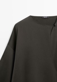 Top grigio scuro in tessuto morbido, con scollo ampio, maniche larghe e dettaglio con bottone sul lato per la chiusura.