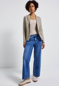 Blazer gris claro, top beige, jeans de pierna ancha azul y zapatillas beige. El material parece suave, con un diseño casual y detalles minimalistas.