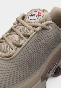 Αθλητικό παπούτσι σε μπεζ και καφέ αποχρώσεις με επάνω μέρος από δίχτυ, μαξιλαρωμένη γλώσσα με ετικέτα "Air Max", μπεζ κορδόνια και υφή στην πλαϊνή επιφάνεια με ορατή αερόσολα απορρόφησης κραδασμών.