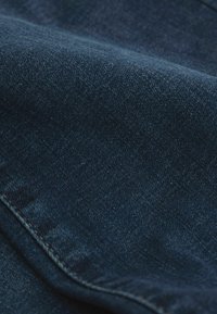 Gros plan sur un tissu en denim bleu foncé montrant la texture et les détails des coutures sur une partie pliée du matériau.