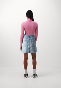 Top rosa fitted a maniche lunghe abbinato a una gonna di jeans leggera blu chiaro con orlo sfrangiato e tasche posteriori, indossato con sneaker nere e calzini bianchi.
