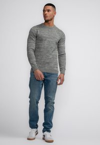 Grey knitted sweater with crew neck, long sleeves, and ribbed hem, paired with light blue jeans and white sneakers with black accents.