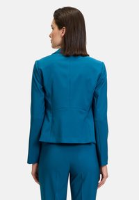 Türkiz fitted zakó strukturált hátsó résszel, egysoros gombolással és testhezálló siluettel, sima, enyhén fénylő anyagból készült.