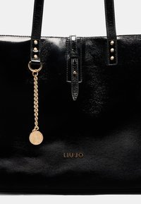 Borsa a spalla in pelle verniciata nera con due manici, dettagli in metallo dorato, catena decorativa e logo del marchio impresso sul davanti.