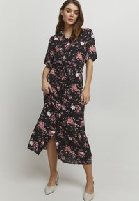 Robe noire à fleurs avec des manches courtes, une taille nouée et une fente sur le côté, faite en tissu léger avec une texture lisse.
