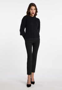 Pulover negru din tricot cu model cable-knit, cu un guler din nervuri și mâneci lungi, purtat împreună cu pantaloni negri slim și pantofi cu vârful ascuțit negri.