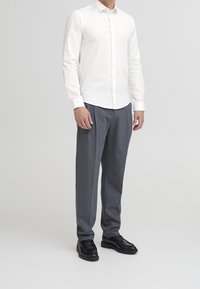 Witte lange mouwen blouse, grijze pinstriped broek en zwarte leren schoenen. Eenvoudig ontwerp met een getailleerde pasvorm.