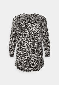 Svart långärmad blus med små vita blommor, rund halsringning och ett nyckelhålsknapppdetalj fram.