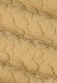 Tissu matelassé d'une teinte jaune doux, présentant un motif texturé de formes arrondies avec des détails de couture visibles. Fini de surface lisse.