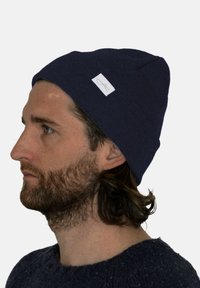 Marineblauer Strickmütze mit eng anliegender Passform und umgeschlagenem Bund, ausgestattet mit einem kleinen weißen aufgenähten Etikett an der Seite. Weiche Textur und einfaches Design.